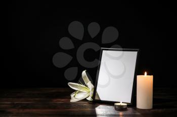Photo frame with lily flower and candles on table against dark background�