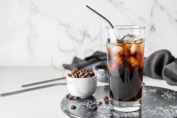 Board with glass of cold brew and coffee beans on light background�