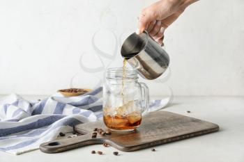 Pouring of cold brew coffee into mason jar on white background�
