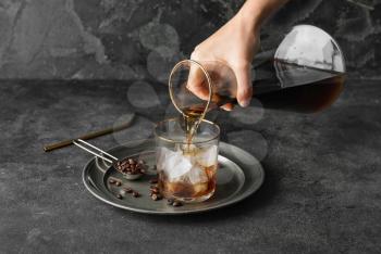 Pouring of cold brew coffee from jug into glass on grunge background�