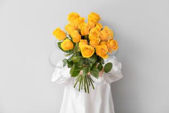 Young woman with beautiful yellow roses on light background�