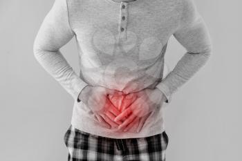 Young man suffering from abdominal pain on light background�