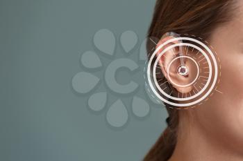 Young woman with hearing aid on grey background�