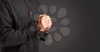 Young priest praying to God on dark background�