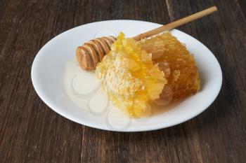 Golden honeycomb and honey stick on a white plate  on vintage wooden table