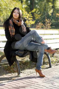 Pretty young woman sitting on a bench in autumn park