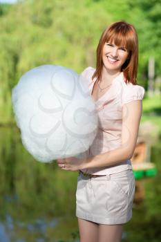 Smiling red-haired woman wearing short skirt and holding a cotton candy