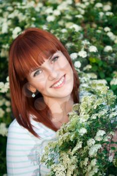 Red-haired smiling woman posing near the flowering bush