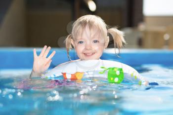 Little blond girl swimming in water pool on inflatable circle