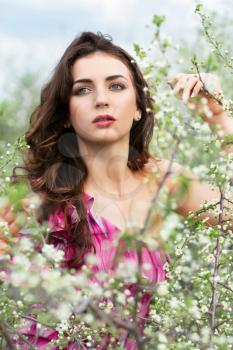 Thoughtful young curly brunette posing in flowering trees