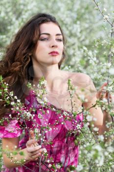 Young thoughtful brunette touching branches of flowering tree