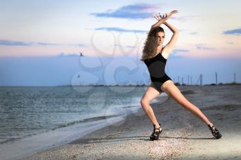 Beautiful leggy brunette posing on the beach in black swimsuit