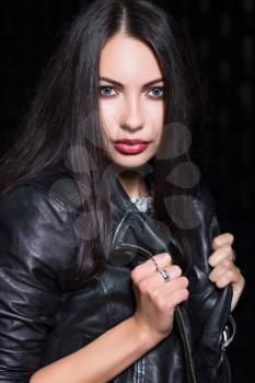 Portrait of young black-haired woman posing in leather jacket. Isolated