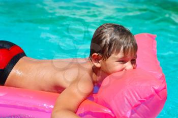 Smiling boy lies on pink mattress in the pool
