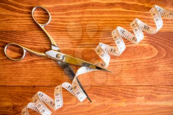 Scissors cutting tape measure on wooden background, concept for slimming