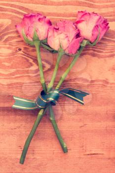 Three dried roses with bow on wooden background. Vintage style.