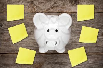 Piggy bank with yellow sticky notes on wooden background