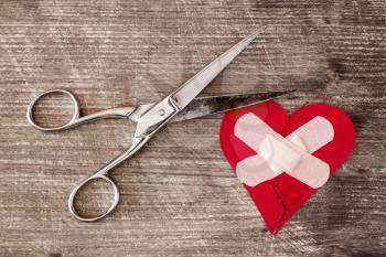 Broken heart with bandage and scissors on a wooden background