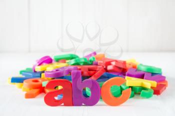 ABC spelling and pile of colorful plastic letters on white wooden background