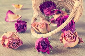 Dried roses flower buds in wicker basket on wooden background