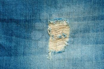 Hole and threads on denim jeans. Ripped  blue jeans background. Close up blue jeans texture.