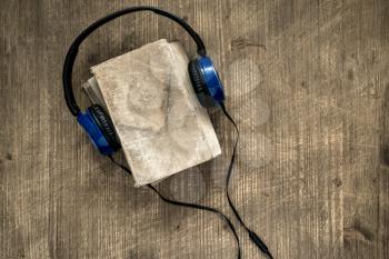  Audio books concept. Headphones put over book with empty cover on wooden background, top view, copy space