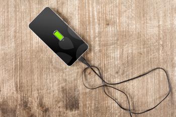 Mobile smartphone charging on wooden desk