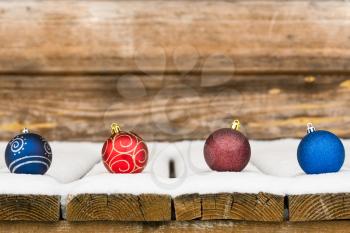 Four Christmas bauble in the snow on wooden background