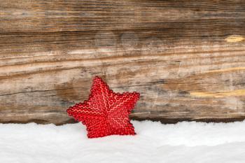 Red Christmas decorations star in the snow against wooden background