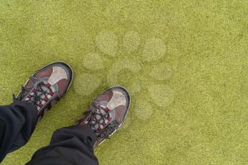 Legs with hiking shoes at artificial green grass playground 