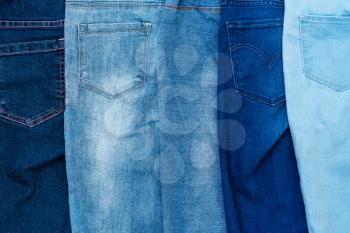 Textured background of a variety of denim pants in various shades of blue stacked in row