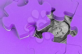 US dollar banknote hidden under purple puzzle. Financial or economic concept