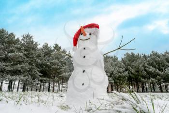 Funny snowman in Santa hat on snowy field. Winter wonderland with a funny smiling snowman in a snowy park.