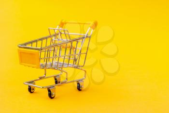Empty shopping trolley on the yellow background. Copy space.