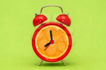 Creative alarm clock with orange fruit on color background