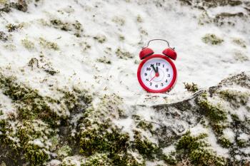 Alarm clock on a snow covered rock. Time freezing concept.