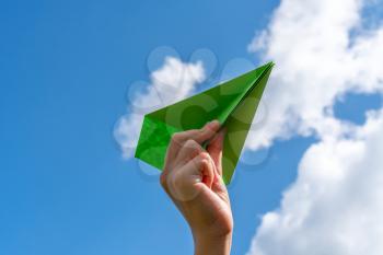 Child hand with green paper plane against blue sky