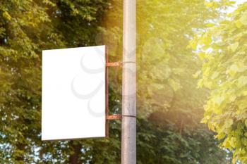 The blank advertising banner suspended on the street lamp pole with the sunlight from the tree background.