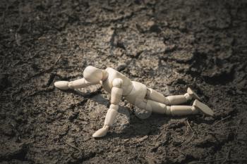 Wooden man lying on cracked earth in the arid area. Thirst and dehydration.