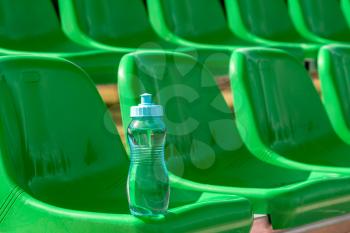 Sport water bottle on the green seats of stadium. Thirst and water balance concept.