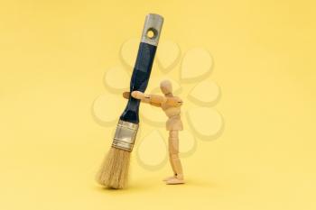 Wooden painter holding big paintbrush on the yellow background