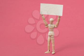 Wooden dummy holding blank placard on the pink background