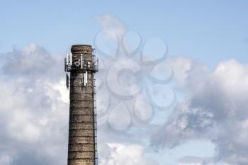 High industrial chimney with multiple antennas on cloudy sky background. 