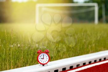 Red alarm clock on the football field with empty gate on background