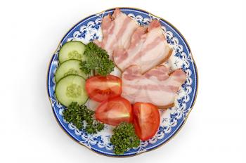 Slices of bacon with slices of cucumbers, tomatoes and sprigs of green parsley on porcelain plate isolated on a white background