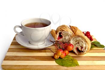 Tea in a white cup, broke a croissant with jam, a sprig of wild apples, viburnum with leaves on a wooden board isolated on white background