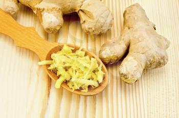 Wooden spoon with grated ginger, ginger root against a wooden board
