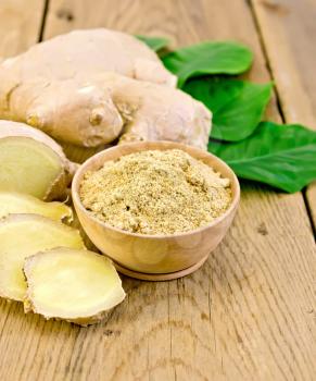 Ginger powder in a bowl, ginger root, green leaves on the background of wooden board