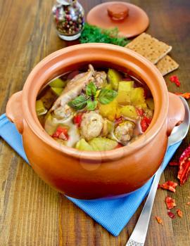 Roast with chicken meat, potatoes and red pepper in a clay pot, blue napkin, spoon, crispbreads, dill and pepper in a jar on a wooden board