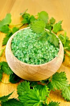Green bath salt in a wooden bowl with nettles on a wooden board